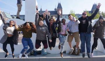 Group of tourists jumping in front of large letters in a city.