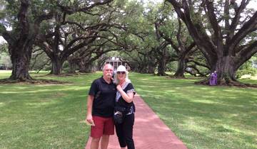 Couple posing under oak trees leading to a house.
