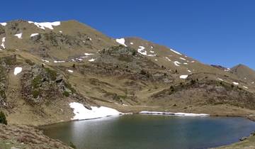 Mountain lake with patches of surrounding snow under clear blue skies.