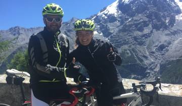 Cyclists posing with thumbs up, snow-capped mountains in the background.