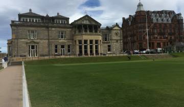Elegant stone building with a grassy foreground and a vibrant brick building in the background.