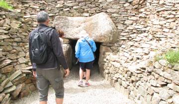 People entering a prehistoric stone structure surrounded by rock walls.