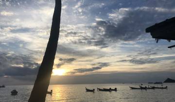 Silhouetted boats on water under a partially cloudy sunset sky.