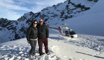 Couple standing on a snowy mountain with a helicopter in the background.