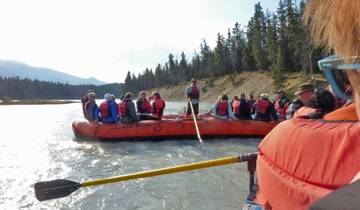 Group of people on a rafting boat in a river surrounded by trees.