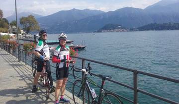 Two cyclists posing by a lake with mountains in the background.