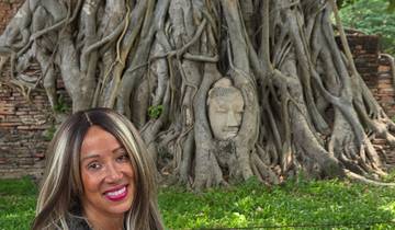 A woman sitting by a Buddha head embedded in a tree.