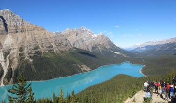 Turquoise lake surrounded by mountains, with people viewing from a vista point.