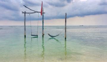 Swing and hammock over calm turquoise water.