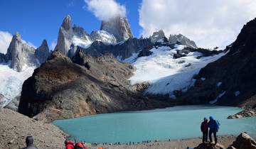 Two hikers near a glacial lake with mountains.