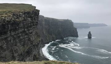 The Cliffs of Moher on a cloudy day with waves crashing below.