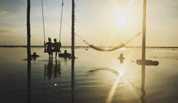 Silhouettes of people on swings in water at sunset