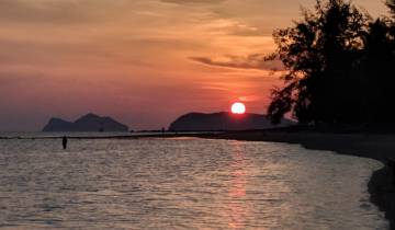 Sun setting over the sea with silhouetted landscape