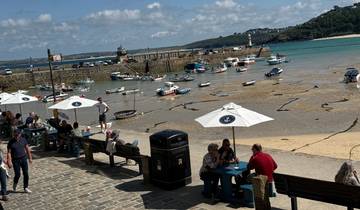 Harbor with boats and people sitting on a bench with an umbrella and stone pavement.