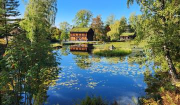 A rural house reflected in a tranquil pond surrounded by trees.