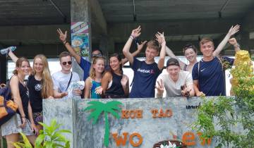 Group of people smiling and cheering with a 'Koh Tao' sign.