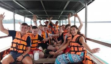 Group on a boat ride wearing life jackets, waving at the camera.