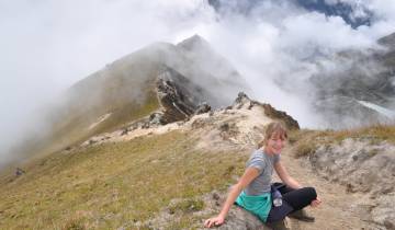 A person sitting on a grassy hilltop with clouds.