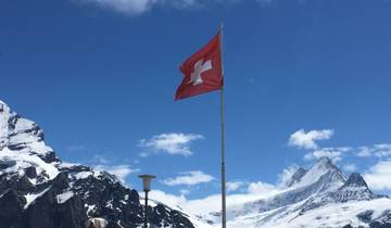 Swiss flag flying over snow-capped mountains.