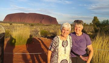 Two people sitting in front of a red rock monolith.