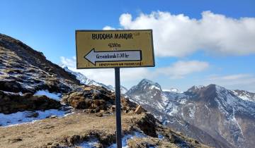 A signpost at Buddha Mandir with snow-covered mountains in the background.