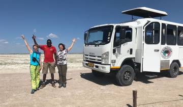 Three people posing next to a safari vehicle with savannah background.