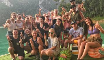 A group of friends posing in front of a lake with a mountainous backdrop.