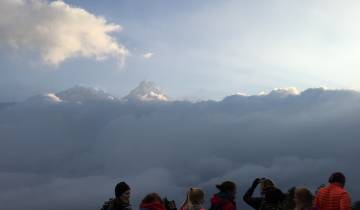 People observing a scenic view of mountains peeking through clouds.