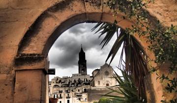 View of Matera framed by an ancient arch with clouds overhead.
