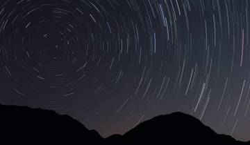 Night sky with star trails above silhouette of hills.