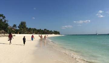 Beach with people walking and boats in the water.