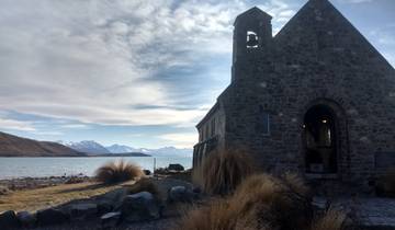Historic stone church by a lake with mountains in the background.