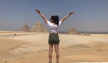 Person raising arms towards pyramids in the desert.
