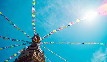 Colorful prayer flags stretched from a stupa under a clear blue sky.