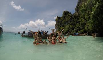 Group posing in the water by longboats at a beach.
