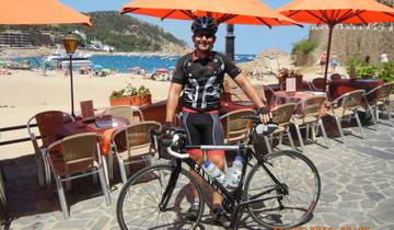 Cyclist posing with a bicycle by the beach with umbrellas in the background.