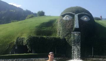 Large grass-covered sculpture with a fountain, woman posing in front.