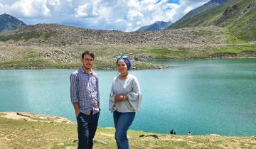 Two people posing in front of a lake with mountains in the background.