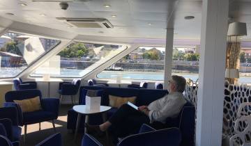 Man sitting in a modern interior of a boat with a river view.