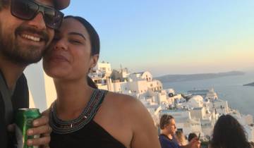 Couple at a scenic viewpoint with the sea and white buildings in the background.