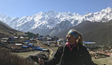 Woman standing with mountains and village in the background.