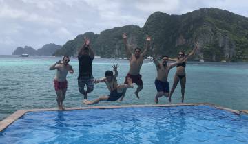Group of people jumping into a pool with the sea in the background.