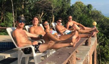 Group of people lounging by a pool with lush greenery in the background.