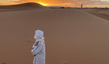 Person in traditional attire standing in a desert at sunset.