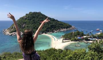 Woman with arms raised looking at a tropical island.