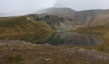 Alpine lake surrounded by rugged mountains and misty skies.