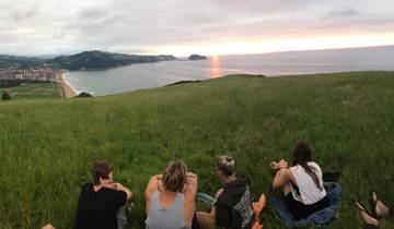 People sitting on a hill enjoying a sunset view over the ocean.