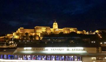 Illuminated cityscape at night with a large building by the river.