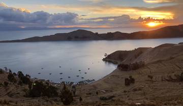 Sunset over a lake with boats and hills.