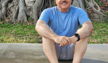 Person sitting in front of a Buddha head entwined in tree roots.